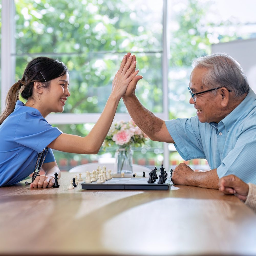 Caregiver takes care of elderly retirement sitting and play chess together think on strategy to win